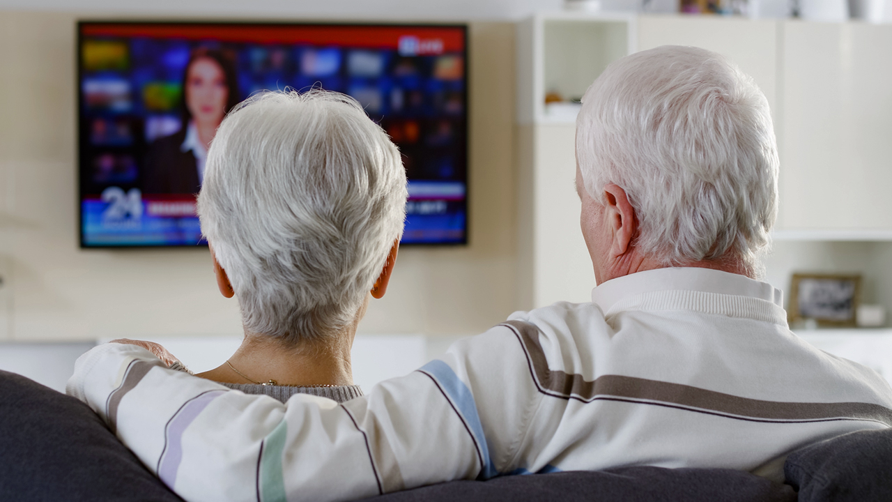A photo of a couple watching local news on TV.