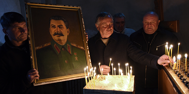 A man holds a portrait of late Soviet dictator Joseph Stalin as others place candles at a church in Stalin's native town of Gori, Georgia, on March 5, 2017, the 64th anniversary of his death. (Vano Shlamov/AFP/Getty Images)