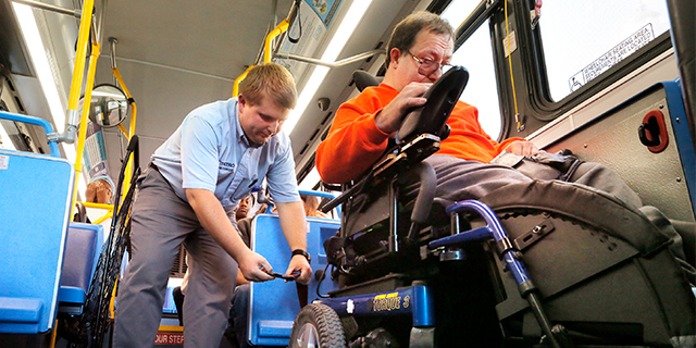 A Metro bus driver fastens a strap to secure a passenger's wheelchair in Portland, Oregon. (Gregory Rec/Portland Press Herald via Getty Images)