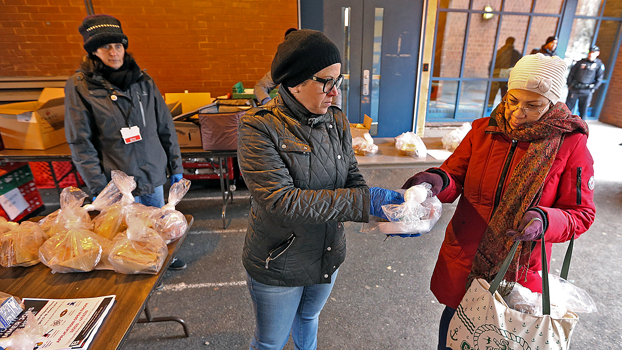 An elementary school cafeteria manager hands a woman free breakfast and lunch meals for her grandchildren on March 17 in Boston. Schools there are closed amid the COVID-19 outbreak. (Matt Stone/MediaNews Group/Boston Herald)
