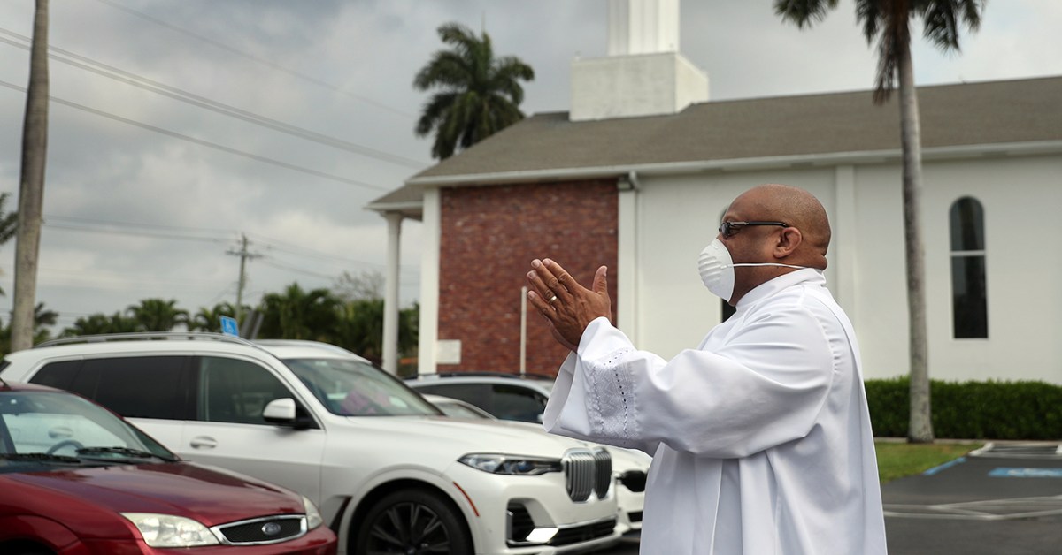 A religious leader greets parishioners arriving for Easter worship in Florida. In order to observe social distancing guidelines, members of the congregation met in the parking lot and watched a Facebook Live streaming of the service taking place inside the church. (Joe Raedle via Getty Images)