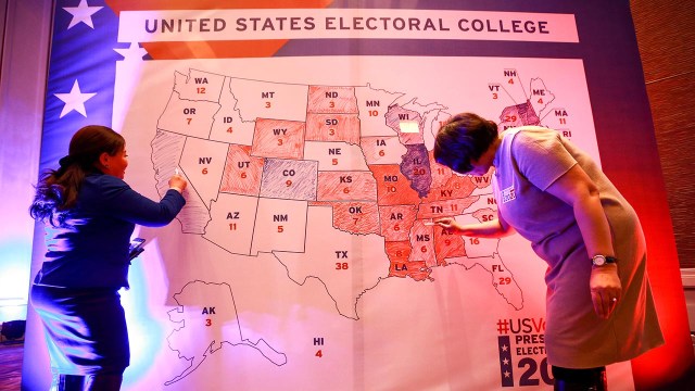 Two people fill in a map of the U.S. that is color-coded by Electoral College results.