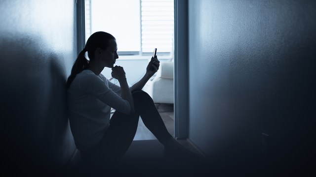 A woman sitting in a hallway and holding her smartphone. (kieferpix via Getty Images)