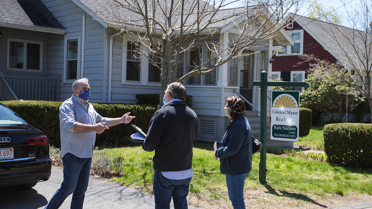 Rick Nazarro z Colonial Manor Realty rozmawia z parą zainteresowanych kupujących czekających na wejście do nieruchomości w maju 2, 2020, w Revere, Massachusetts, na otwarty dom przeprowadzony zgodnie z protokołami COVID-19. (Blake Nissen dla The Boston Globe via Getty Images)