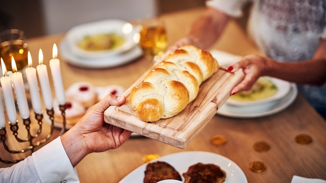 A family gathers around the table sharing challah. (macniak via Getty Images)