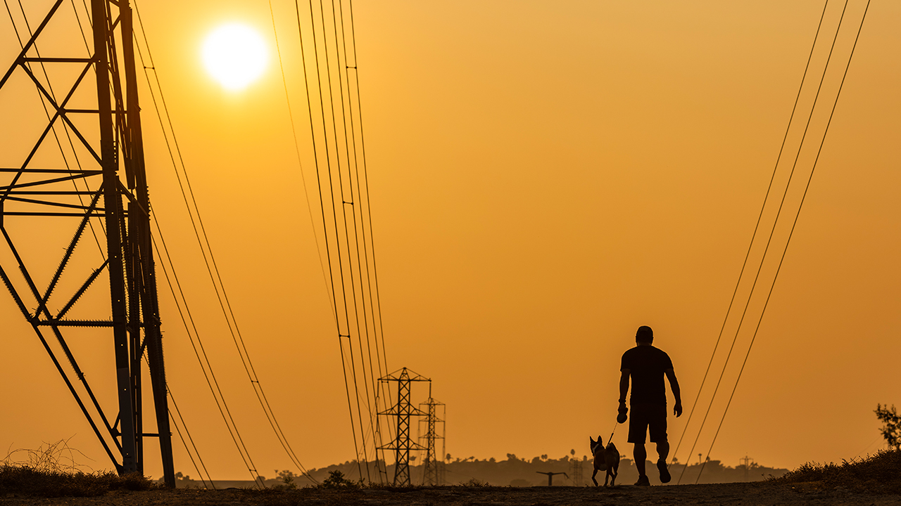 Заполненное дымом небо отливает оранжевым оттенком на закате, когда мужчина и его собака гуляют в Лагуна-Хиллз, Калифорния, 16 сентября 2020 года.