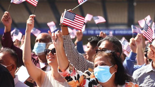 New U.S. citizens wave American flags after being being sworn in at a naturalization ceremony at Dodger Stadium in Los Angeles on Aug. 29, 2022.