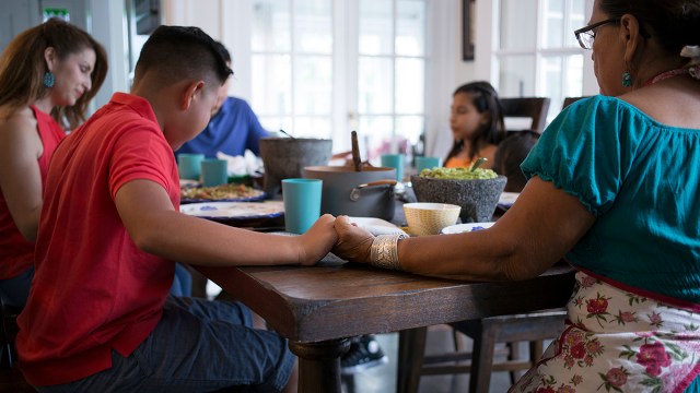 A family saying grace before a meal at dining table (The Good Brigade via Getty Images).