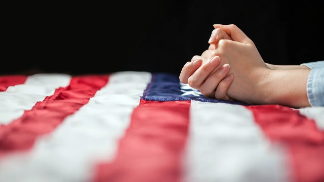Hands praying over an American flag.