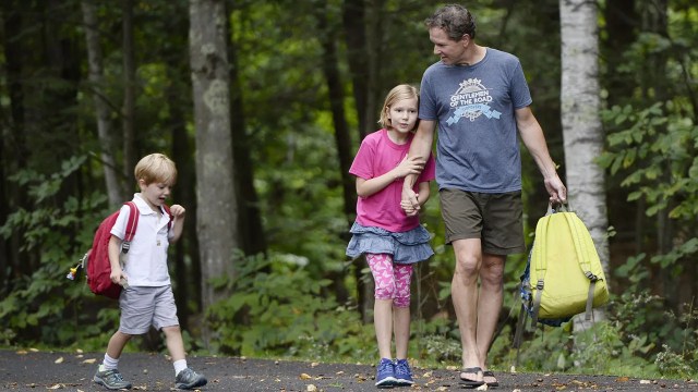 A stay-at-home dad in Falmouth, Maine, walks with his children, ages 5 and 9, after they were dropped off by the school bus. (Shawn Patrick Ouellette/Portland Portland Press Herald via Getty Images)