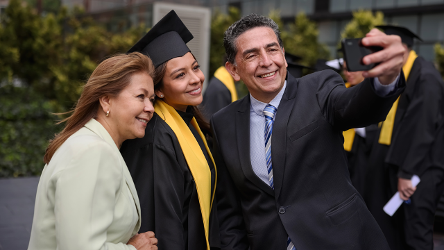 Graduate student taking a selfie with her parents on her graduation day - stock photo