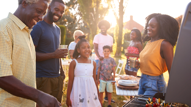 Stock image of a multi-generation black family barbecue, grandad grilling.