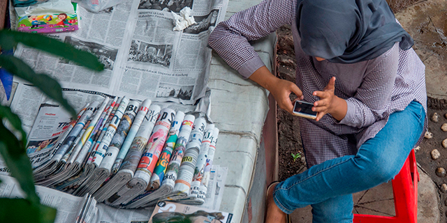 A newspaper vendor uses her smartphone while tending her stall in Jakarta, Indonesia, on Nov. 14, 2017. (Bay Ismoyo/AFP/Getty Images)