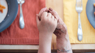 Grandmother and grandson holding hands at dinner table