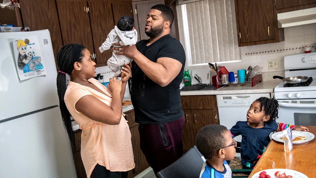 Geri Andre-Major passes her 2 1/2-week-old son, Maverick, to her husband, Mo Major, as their other children Max, 5, and Marley, 4, eat breakfast on March 26, 2020, in Mount Vernon, New York. Both parents lost their jobs due to the coronavirus pandemic. (John Moore/Getty Images)