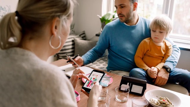 A man sits with a child on his lap while looking at a cellphone, and a woman also seated at the table checks her cellphone. (Getty Images)