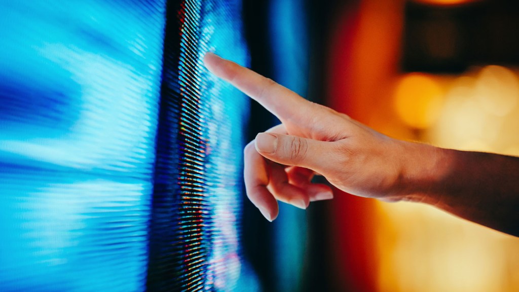 Close up of woman’s hand touching illuminated and multi-coloured LED display screen, connecting to the future. People, lifestyle and technology