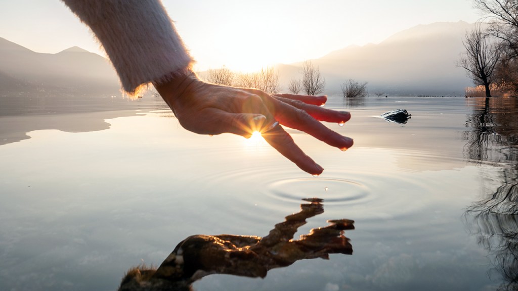 Detail of hand touching water surface of lake at sunset