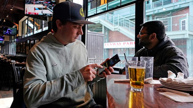A customer at a sports bar near Boston's Fenway Park looks at the mobile betting app on his phone after placing a wager while a men's college basketball game is showing in March 2023. (Charles Krupa/AP File)