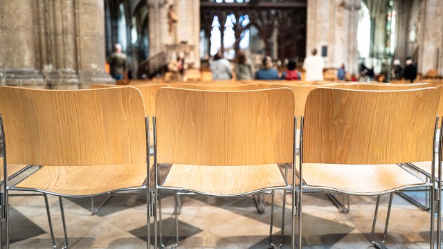 Rows of wooden seats seen on a famous English cathedral, used by congregations of the cathedral. Visitors can be seen in the background.