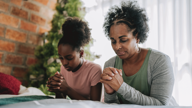 Mother and daughter praying on their knees in their bedroom
