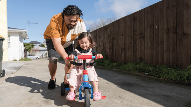 An image a Pacific Islander man teaching his daughter how to ride a bike (nazar_ab via Getty Images)