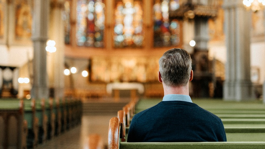 Rear view of mature man sitting on pew while praying at protestant church