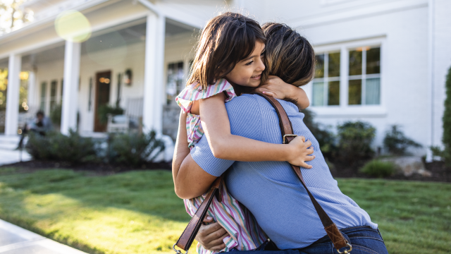 An image of a Latina mother and young daughter embracing in front of suburban home