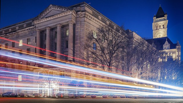 An image of Traffic along Pennsylvania Avenue streaks by the Internal Revenue Service (IRS) headquarters building at night. (Photo by J. David Ake/Getty Images)