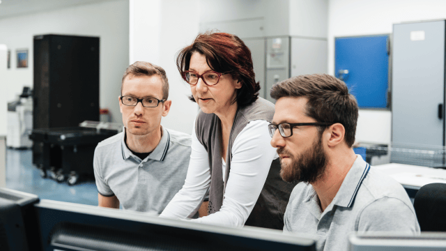 Stock photo of a woman talking with two male programmers.